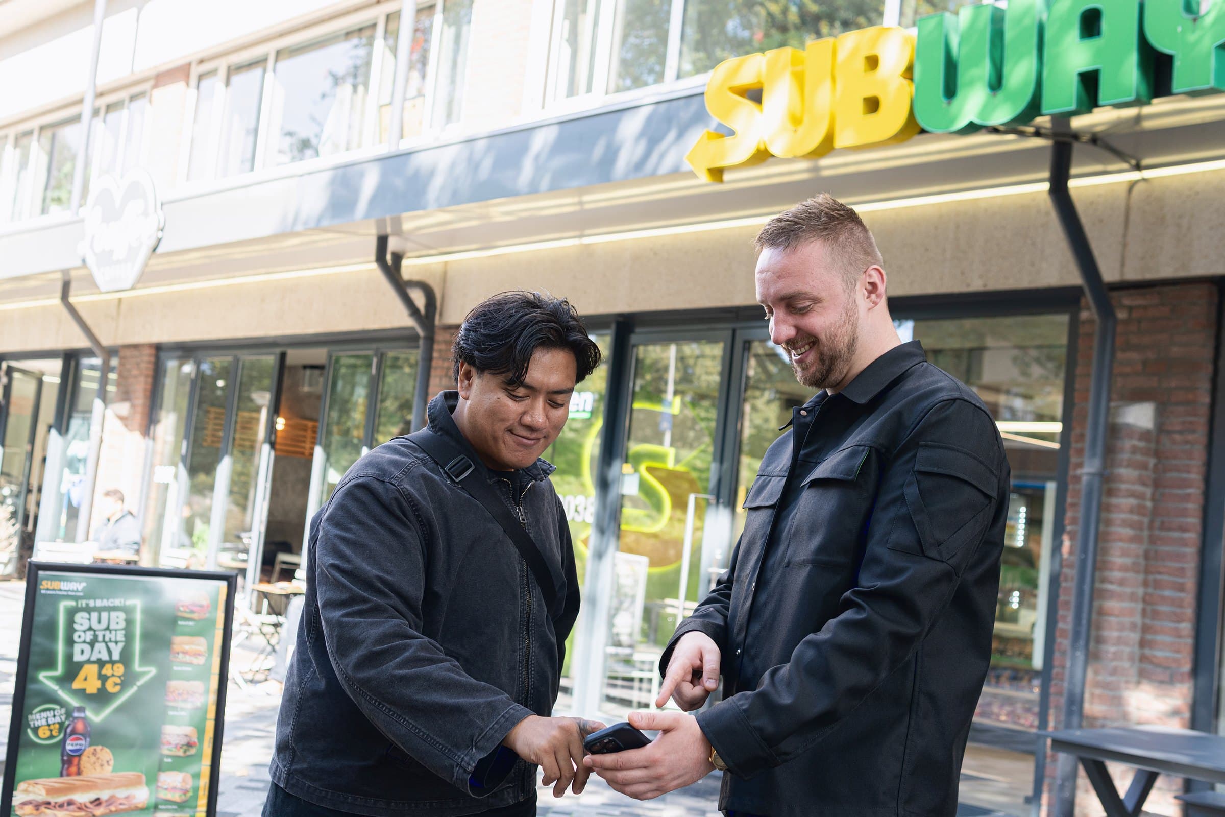 Twee ondernemers bekijken samen een energievoorstel op een telefoon, voor een zaak in de binnenstad