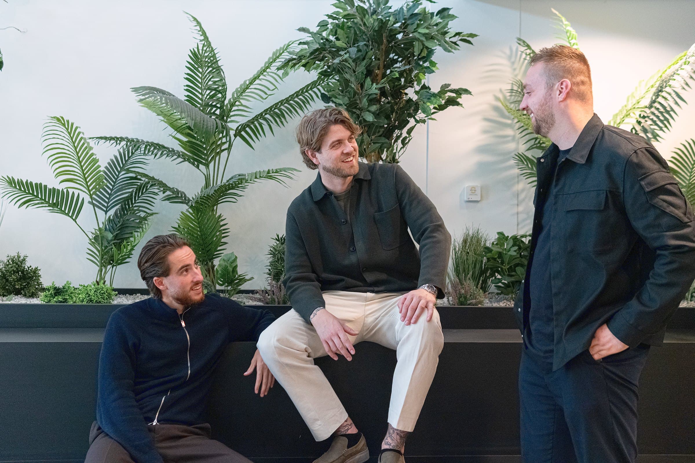 Drie mensen in een ontspannen gesprek bij de plantenwand op kantoor